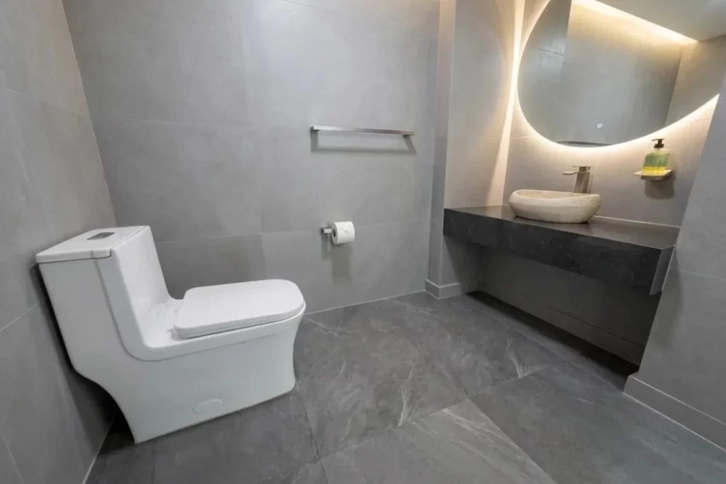 Baño remodelado en Los Cortijos Caracas, Venezuela, con espejo circular iluminado y lavamanos de piedra - Empresa de Remodelaciones en Caracas